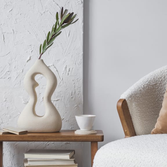 a table with books and a vase on it next to a bed