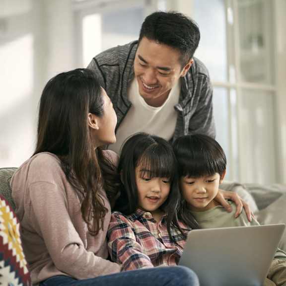 A family of four is sitting on a couch with a laptop.