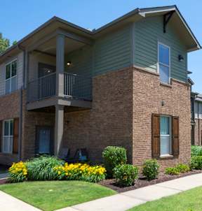 A brick building with a balcony and a small garden in front. at Hall Creek Apartment Homes, Arlington, Tennessee