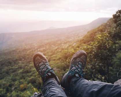 A person's feet in hiking boots are resting on a rock with a scenic view of a valley below.