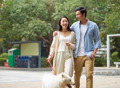 A man and woman walking a white dog in a park.