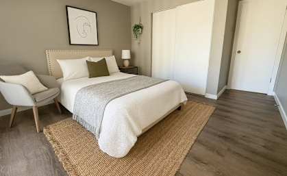 A bedroom with a bed, chair, and a rug.