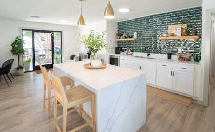 A kitchen with a white marble island and wooden chairs.