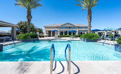A swimming pool surrounded by palm trees and a building in the background. at Vistoria At Marley Park Apartments, Arizona
