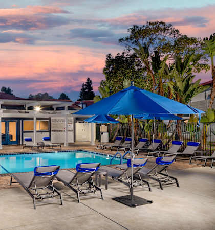 A poolside area with lounge chairs and umbrellas is set against a sunset sky.