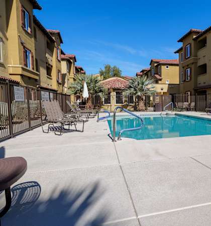 A swimming pool surrounded by a concrete patio and apartment buildings.