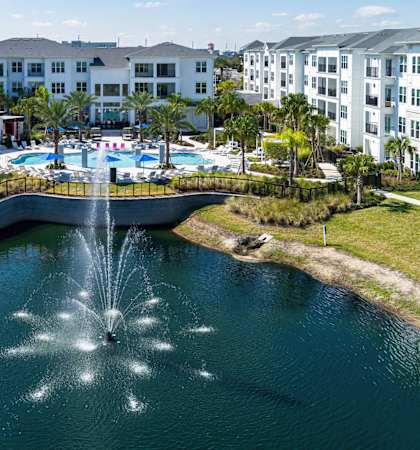 A fountain in the middle of a pond in front of apartment buildings.