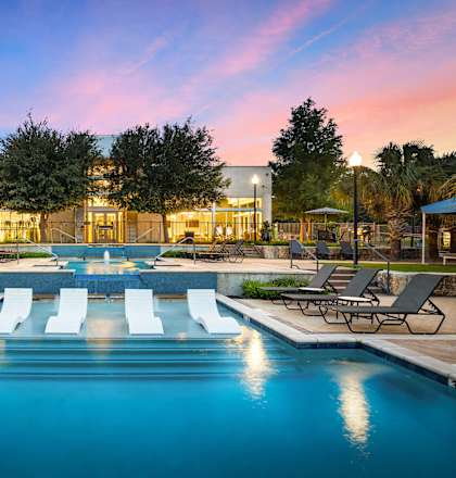 A large swimming pool in front of a building with lounge chairs around it.