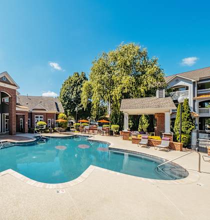 A large swimming pool surrounded by a patio with chairs and umbrellas.