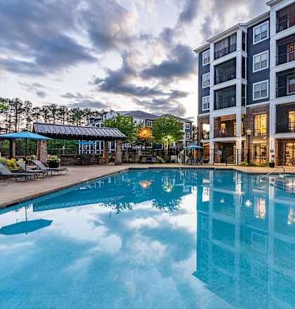 a swimming pool at night with an apartment building in the background