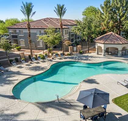 A large swimming pool surrounded by a patio area with chairs and a gazebo.