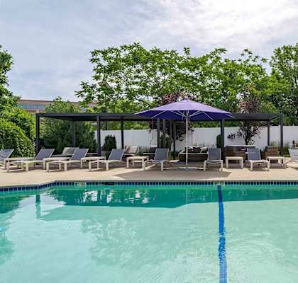 A pool with a blue umbrella and chairs around it.