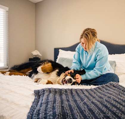a woman sitting on a bed playing with her dog