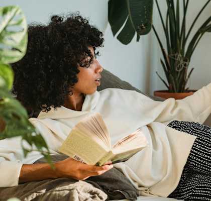 a woman laying on a couch with her dog and reading a book