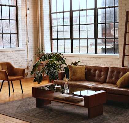 a loft living room with a leather couch, coffee table, decor, and large windows