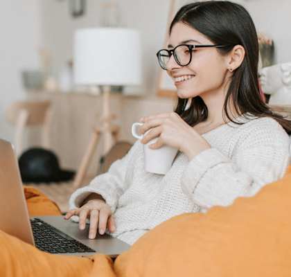a happy woman sitting on a couch with a laptop computer and a cup of coffee