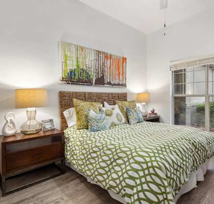 A bedroom with a bed, nightstand, and a painting on the wall.