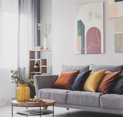 A grey couch with colorful pillows sits in a living room with a coffee table and two paintings on the wall. at Chambers Senior Housing, Kingston, New York
