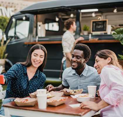 Three people are sitting at a table eating food in front of a food truck.