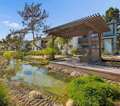A serene pond with a wooden pergola overlooking it.