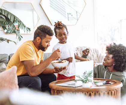 a family sitting in a living room eating food and watching a television