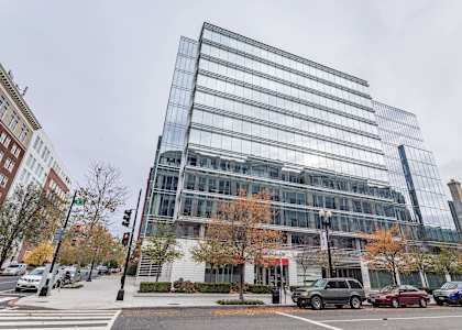 A modern glass building is situated on a street corner with cars parked along the curb.