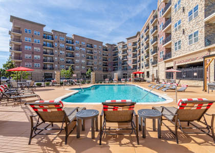 A pool surrounded by chairs and umbrellas in front of apartment buildings.at Carson Street Towers, Overland Park