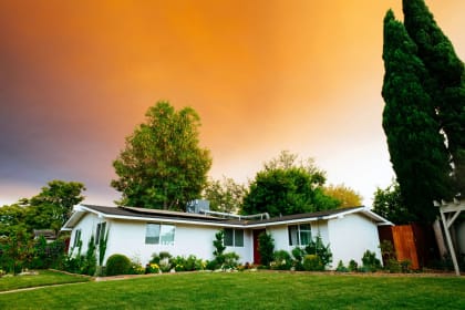 a white house with a lawn and trees under an orange sky