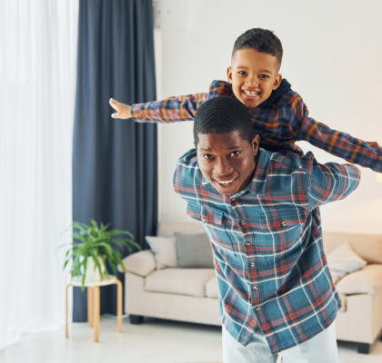 a man with a young boy on his shoulders in a living room