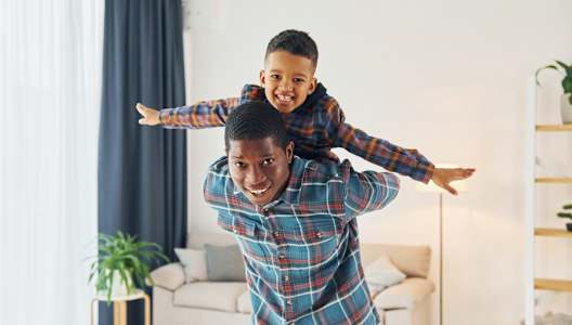 a man with a young boy on his shoulders in a living room