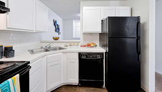 A black refrigerator stands in a kitchen with white cabinets and a black stove.