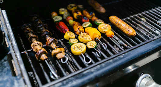 A variety of vegetables and sausages are being grilled on a barbecue.