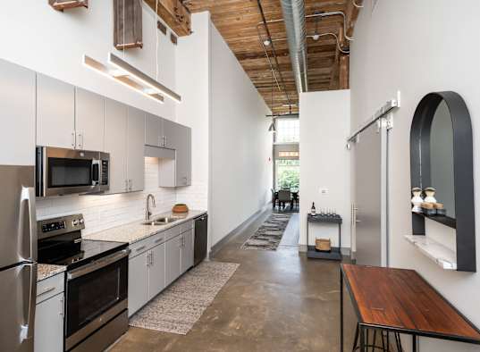 Industrial-style kitchen with high ceilings, stainless steel appliances, and a wooden table.