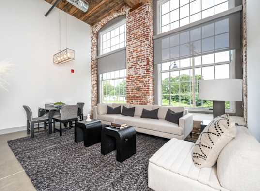 Industrial-style living room with high ceilings, large windows, a couch, and a table.