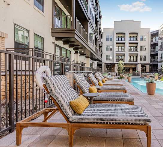A pool area with lounge chairs and a fence.