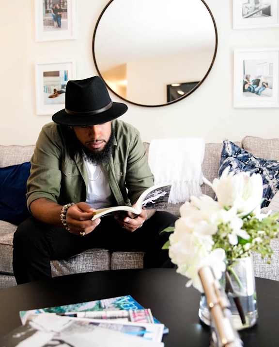 A man in a hat is reading a book on a grey couch at Rosemont Place Apartments, Des Moines, IA, 50320