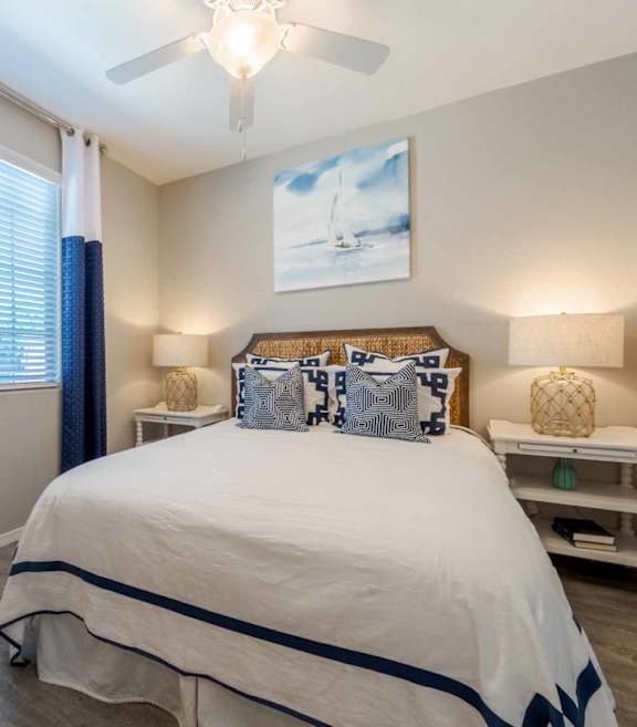 A bedroom with a bed, nightstand, and a plant. at Vistoria At Marley Park Apartments, Arizona
