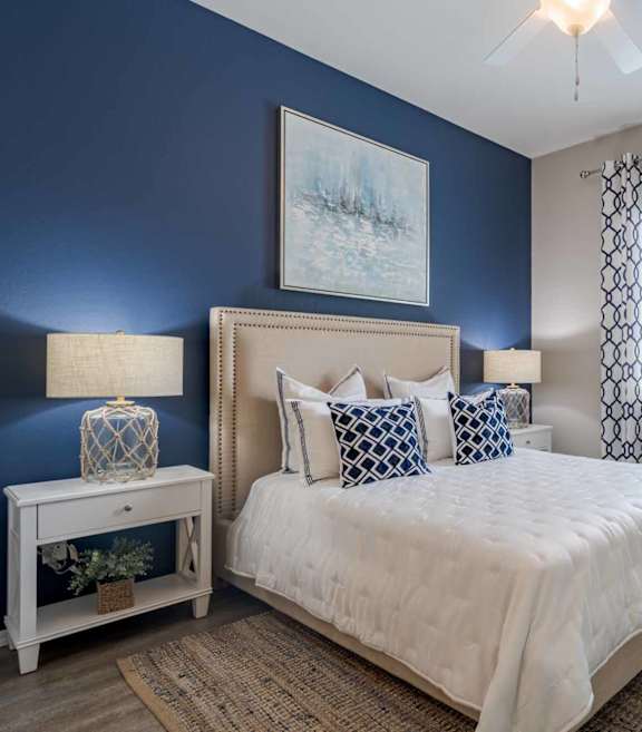 A bedroom with a bed, nightstand, and a plant.