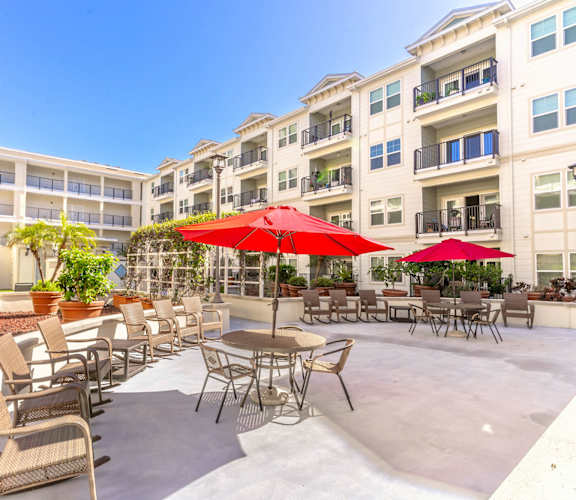a patio with tables and umbrellas in front of an apartment building