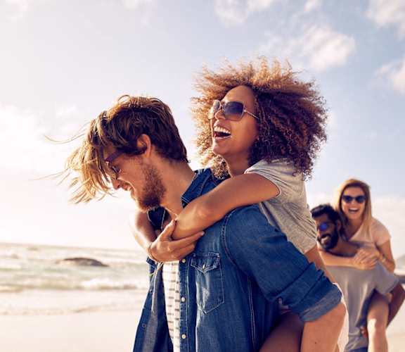 a man carrying a woman on the beach with other people
