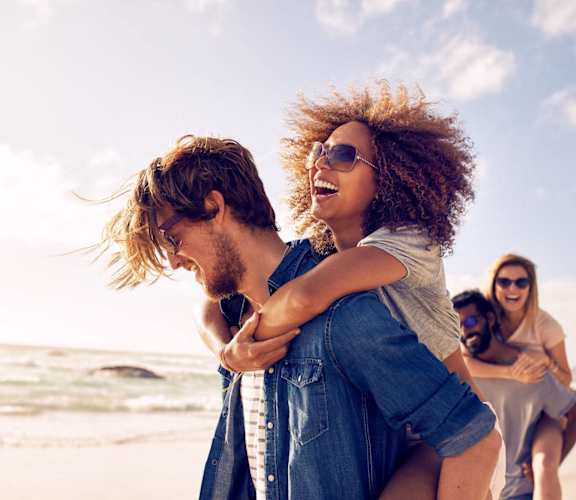 a man carrying a woman on the beach with other people