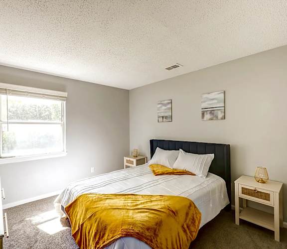 A bedroom with a bed, nightstand, and window at Sedgefield Square Apartments, North Carolina, 27407