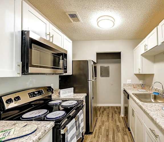 A kitchen with a black stove top oven and a black microwave above it at Sedgefield Square Apartments, North Carolina, 27407