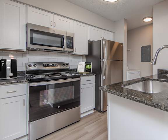 A kitchen with a stove, microwave, refrigerator, and sink.