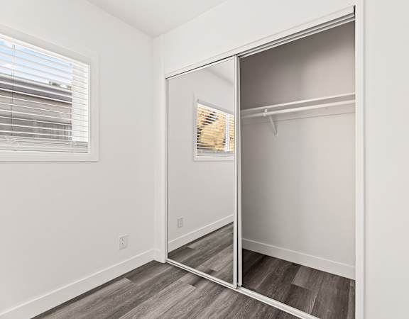 A walk-in closet with a mirror and a wooden floor.