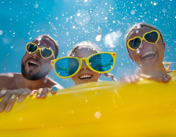 Family of 3 in Yellow Sunglasses Smiling and Hanging Over Edge of Yellow Inflatable Pool Raft 