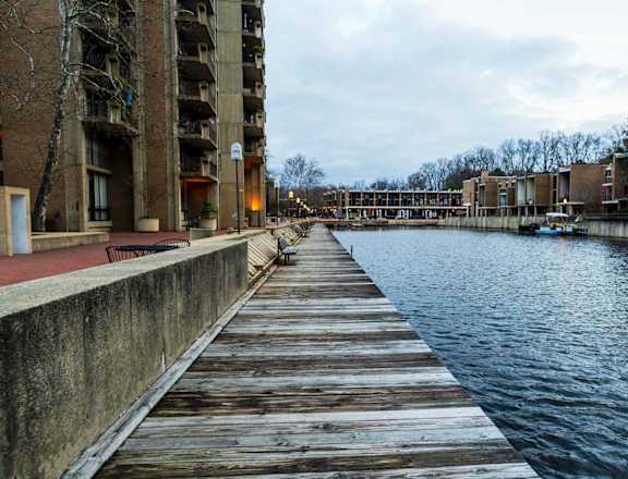 A wooden dock extends into a calm body of water with buildings on either side.