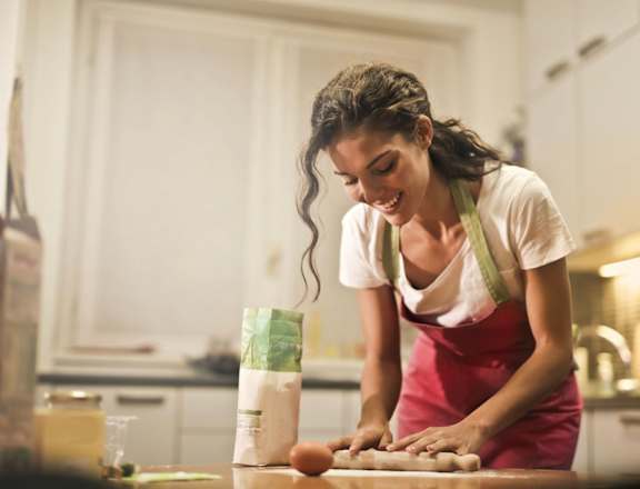 A woman in a red apron is kneading dough on a kitchen counter.