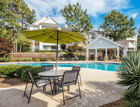 A patio with a table and chairs and a pool in the background.