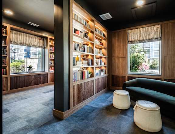 A room with a green couch, a bookshelf, and two poufs.